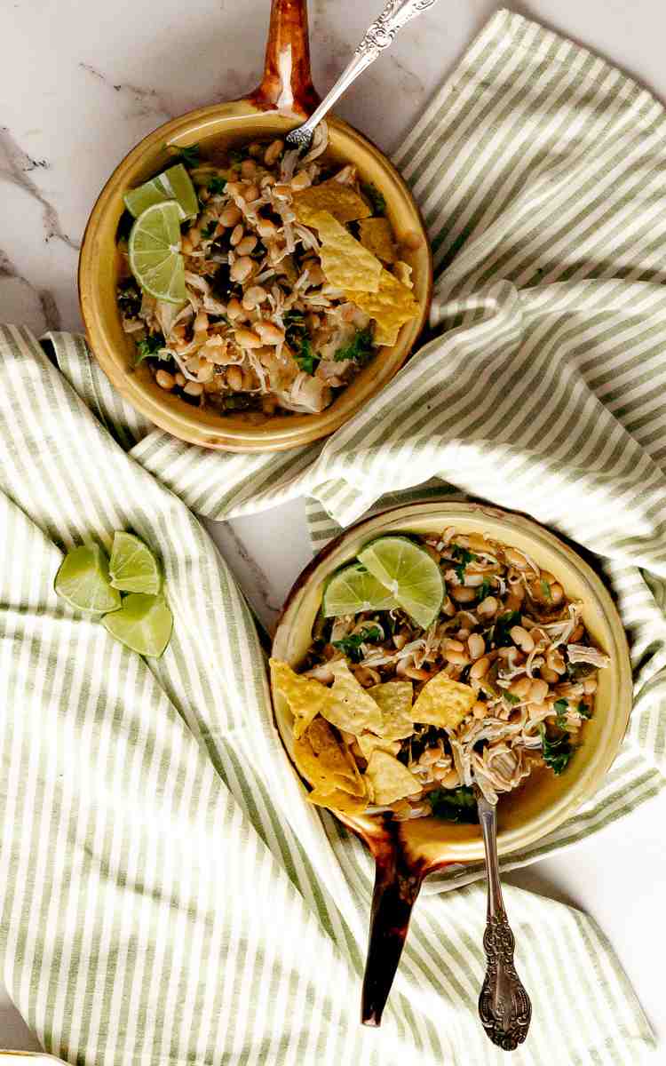 Green Chicken Chili in two bowls with handles and lime wedges.