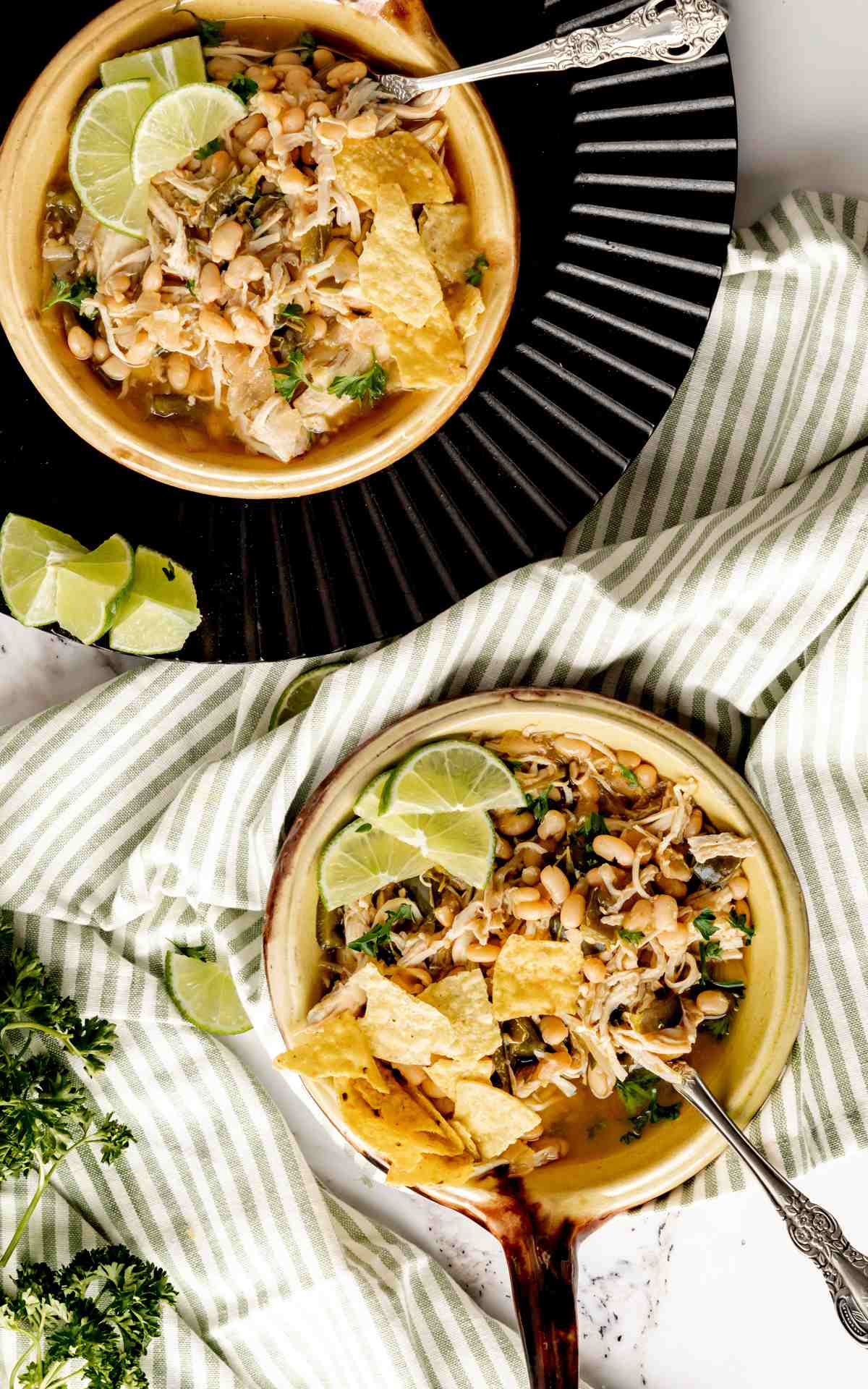 Overhead photo of two bowls of chicken chili with cilantro and tortilla chips.