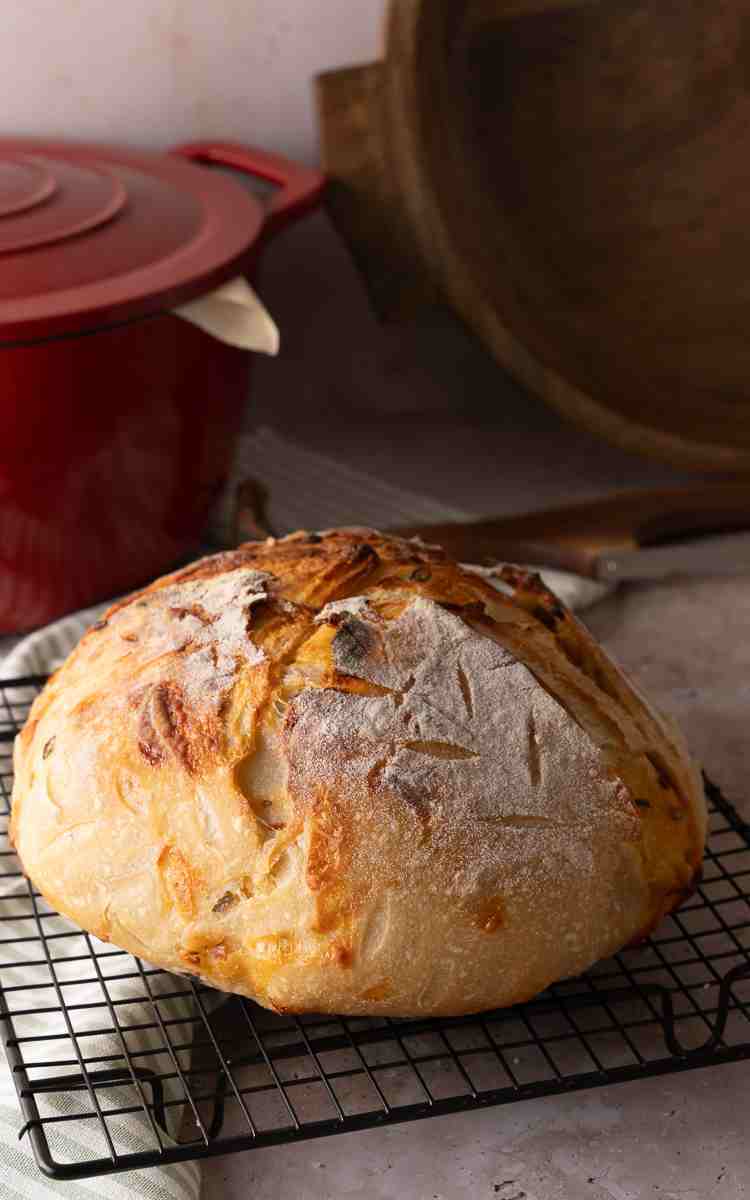 A cheddar jalapeno sourdough bread loaf on cooling rack uncut.