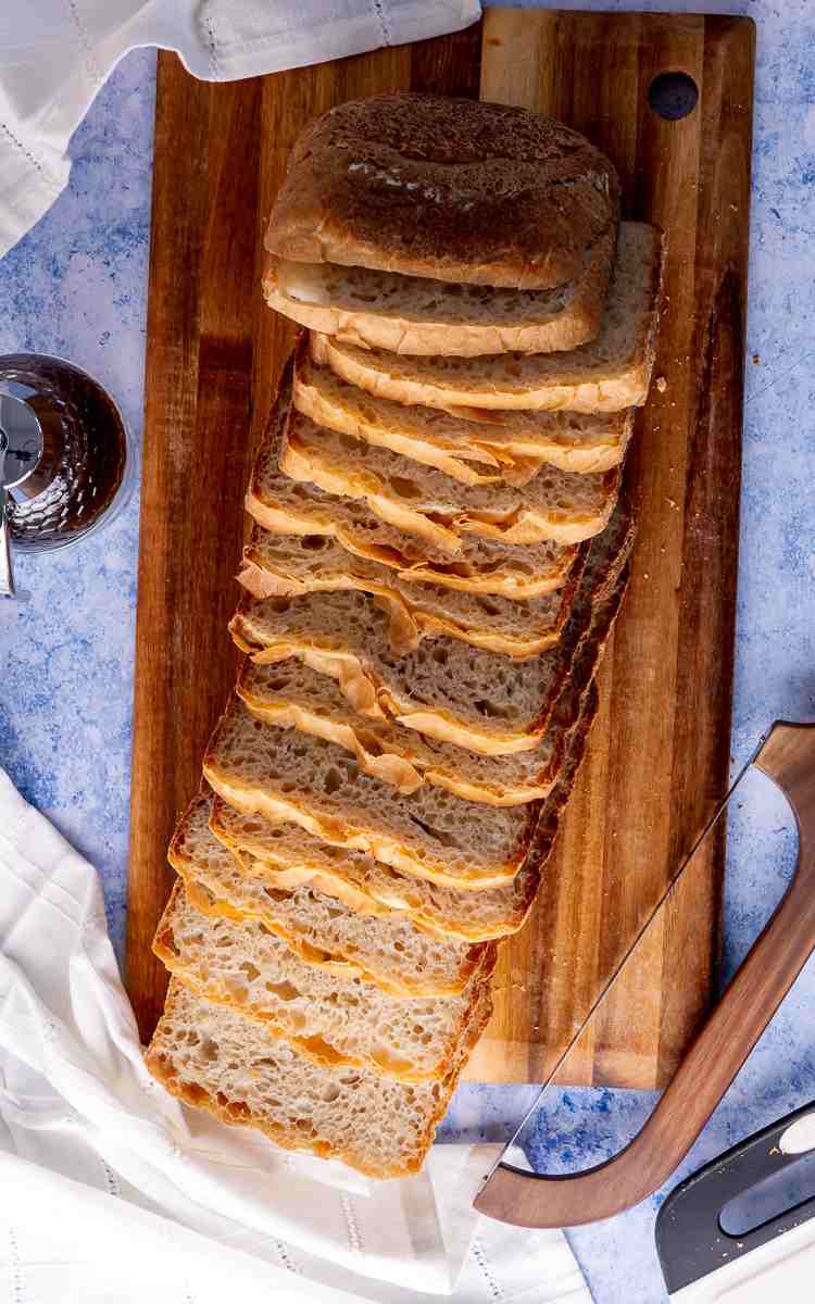 A full loaf of white honey bread on cutting board with bread knife.