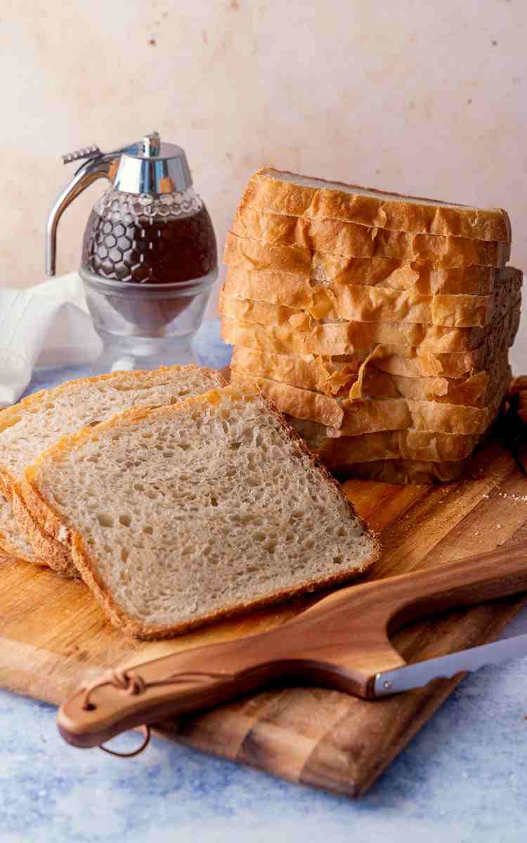Sliced and stacked honey white bread loaf on cutting board.