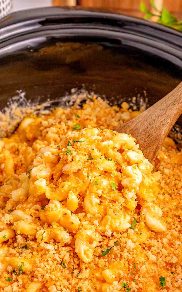 Slow cooker mac and cheese with a wooden spoon scooping it up.