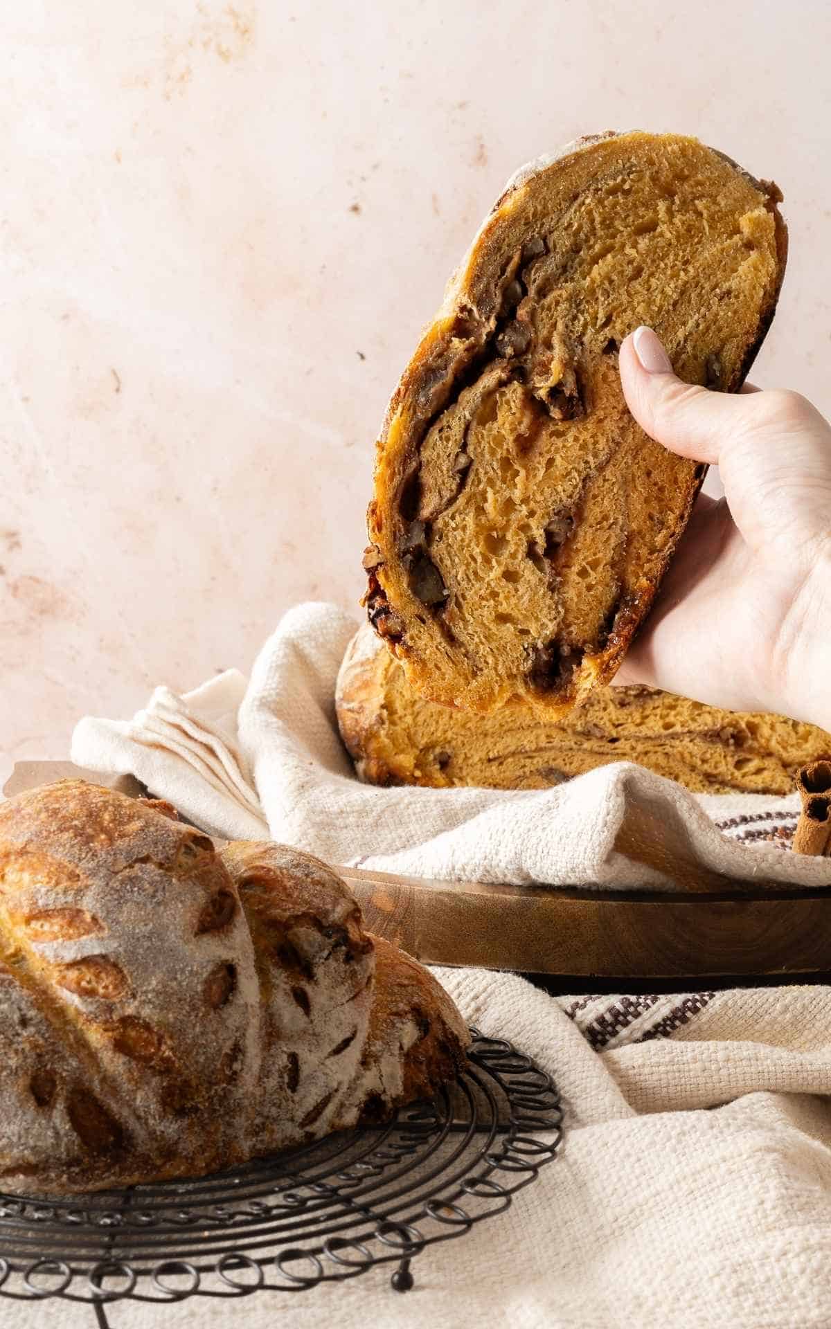 A hand holding up a slice of sourdough pumpkin bread with cinnamon swirl.