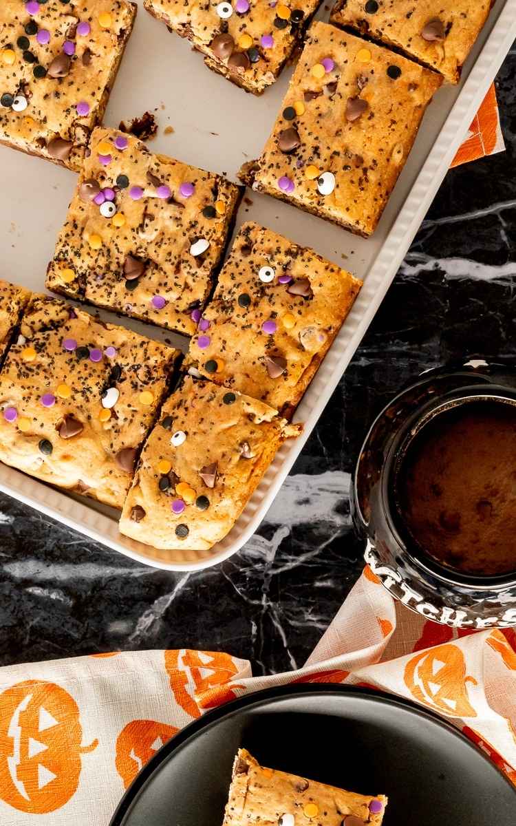 A pan of cut Halloween cookie bars with a cup of hot cocoa.