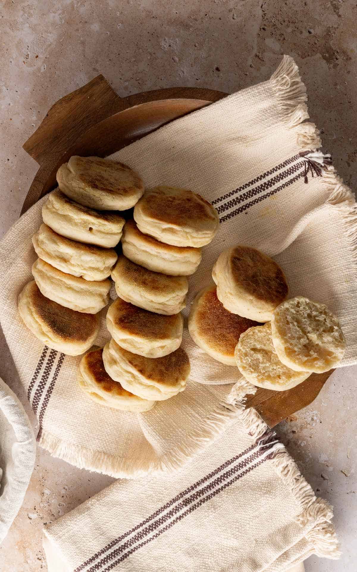 Several sourdough discard English muffins in wooden bowl with linen liner.